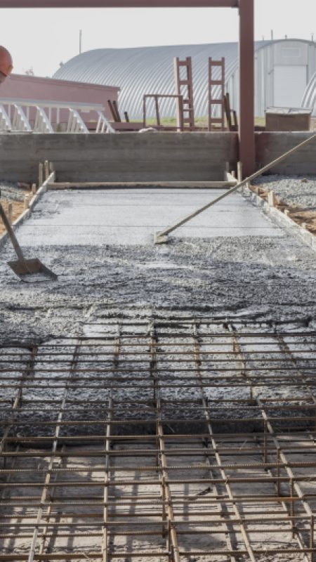 Pouring cement or concrete with a concrete mixer truck, construction site with a reinforced grillage foundation. Workers settle and level the concrete in the foundation